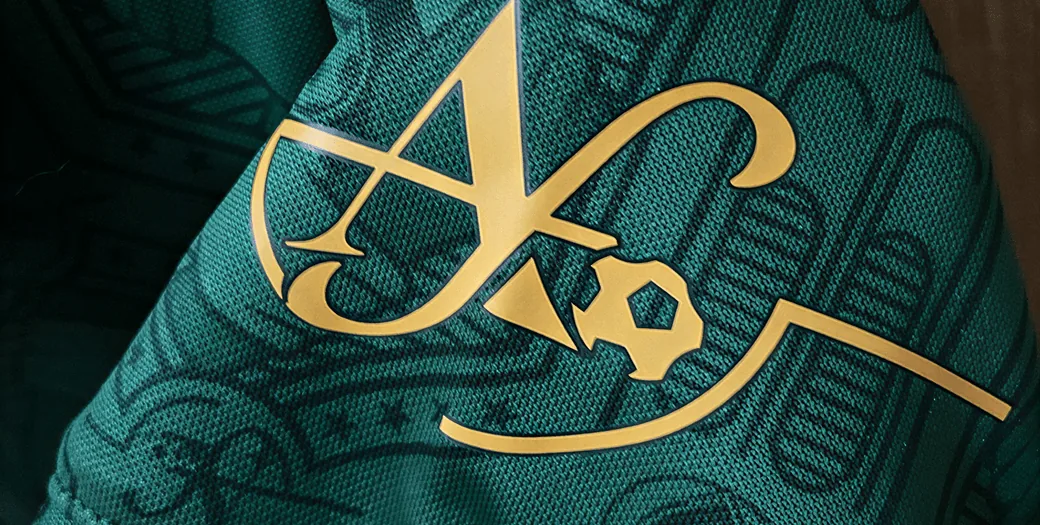 Emblema dourado AF da marca Abel Ferreira aplicado sobre tecido verde