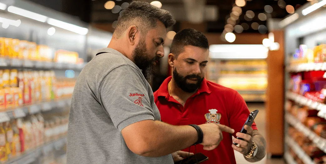 Representante Juntos+ e varejista consultando um celular no ponto de venda